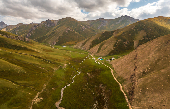 Aerial view of Tash Rabat Caravan Palace in a green valley surrounded by rugged mountains with a winding stream and traditional yurts in At Bashi District Naryn Region Kyrgyzstan. Aerial view of Tash Rabat Caravan Palace in a green valley surrounded by rugged mountains with a winding stream and traditional yurts in At Bashi District Naryn Region Kyrgyzstan.