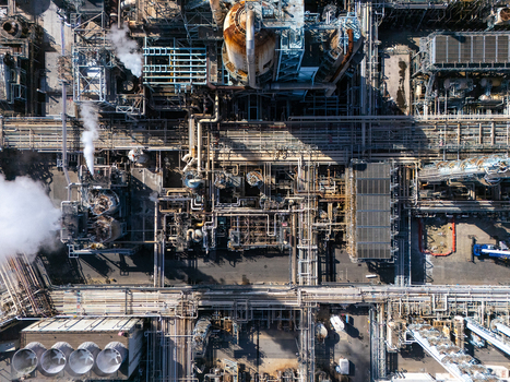 Aerial view of an industrial refinery complex with intricate piping storage tanks and steam rising from processing units in Carson California United States.