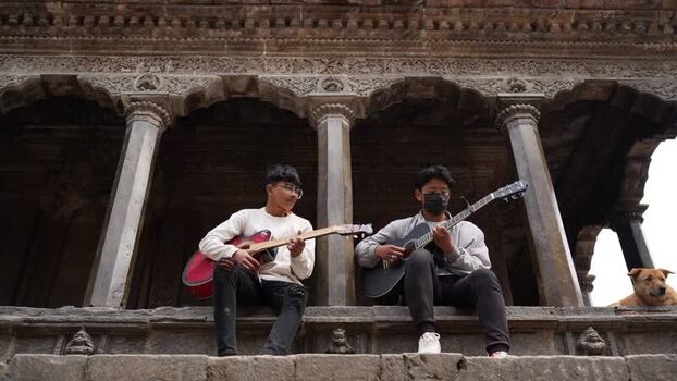 View of two young men playing guitars at a historic temple Nepal.