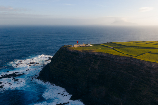 Aerial view of Farol de Albarnaz lighthouse on a steep cliff edge with green pastures and crashing waves in Ponta Delgada Acores Portugal. Aerial view of Farol de Albarnaz lighthouse on a steep cliff edge with green pastures and crashing waves in Ponta Delgada Acores Portugal.