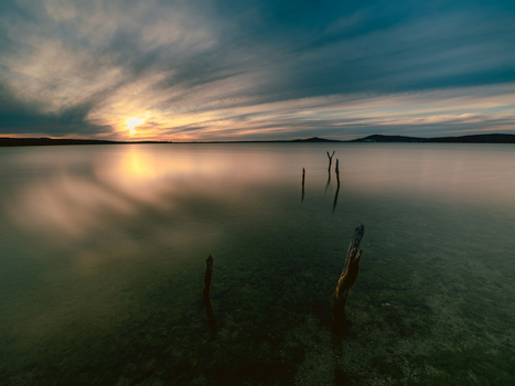 View of the calm waters at sunset with wooden posts protruding from the shallow lake bed under a dramatic sky in Vancouver Peninsula Western Australia Australia. View of the calm waters at sunset with wooden posts protruding from the shallow lake bed under a dramatic sky in Vancouver Peninsula Western Australia Australia.