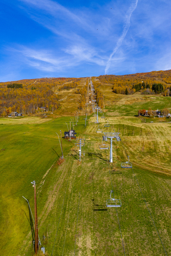 Aerial view of a chairlift extending up a mountainside covered in autumn foliage with green fields and clear blue sky in Bjorli Innlandet Norway. Aerial view of a chairlift extending up a mountainside covered in autumn foliage with green fields and clear blue sky in Bjorli Innlandet Norway.