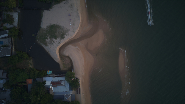 Aerial view of Jomtien Beach featuring a river estuary meeting the sea with a boat wake and coastal buildings in Chon Buri Thailand.