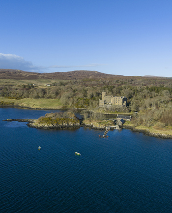 Aerial view of Dunvegan Castle and Gardens on a rocky outcrop overlooking the blue waters of Loch Dunvegan surrounded by lush forests Isle of Skye Scotland United Kingdom. Aerial view of Dunvegan Castle and Gardens on a rocky outcrop overlooking the blue waters of Loch Dunvegan surrounded by lush forests Isle of Skye Scotland United Kingdom.
