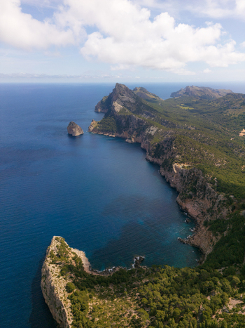 Aerial view of the rugged cliffs of Cap de Formentor overlooking the deep blue Mediterranean sea and lush green forests in Balearic Islands Spain.