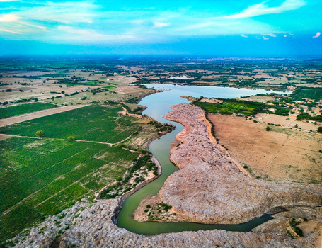 Aerial view of a winding river flowing through lush green agricultural fields and arid landscape in Dera Ghazi Khan Punjab Pakistan.