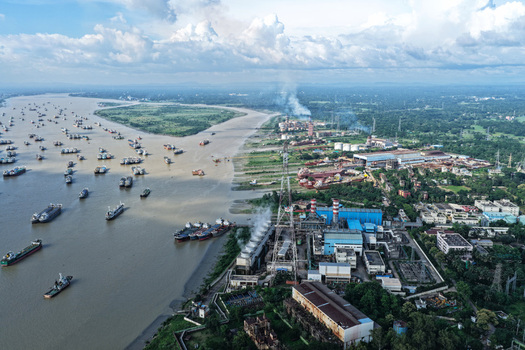 Aerial view of the Karnaphuli River featuring numerous cargo ships and industrial facilities with smoke stacks along the riverbank in Chattogram Chittagong Division Bangladesh.