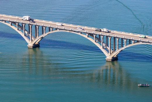 Aerial view of the Isaac Lee Patterson Bridge spanning the blue waters of the Rogue River with vehicles driving across the concrete arches in Gold Beach Oregon United States. Aerial view of the Isaac Lee Patterson Bridge spanning the blue waters of the Rogue River with vehicles driving across the concrete arches in Gold Beach Oregon United States.
