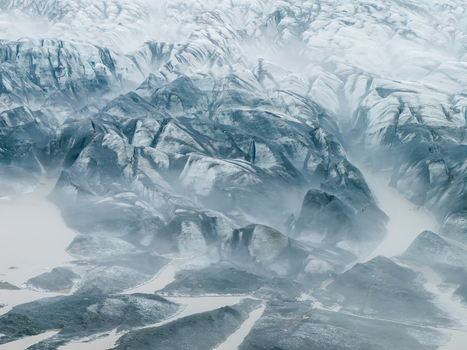 Aerial view of a rugged glacier with dark volcanic rock formations white ice and glacial meltwater streams flowing through the landscape in Iceland. Aerial view of a rugged glacier with dark volcanic rock formations white ice and glacial meltwater streams flowing through the landscape in Iceland.