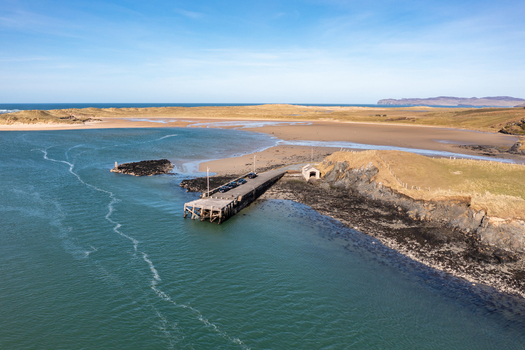 Aerial view of Ballyness Bay featuring a concrete pier extending into the turquoise water surrounded by sandy beaches grassy dunes and rugged coastline in Ballyness County Donegal Ireland. Aerial view of Ballyness Bay featuring a concrete pier extending into the turquoise water surrounded by sandy beaches grassy dunes and rugged coastline in Ballyness County Donegal Ireland.