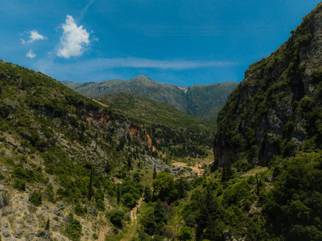 Aerial view of a deep green valley nestled between rugged rocky mountains and steep cliffs under a clear blue sky Dhermi Vlore County Albania. Aerial view of a deep green valley nestled between rugged rocky mountains and steep cliffs under a clear blue sky Dhermi Vlore County Albania.