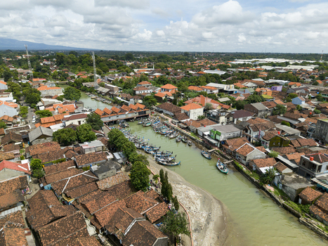 Aerial view of boats clustered at the floating fish market a vibrant scene of commerce amidst the red tiled rooftops and lush greenery Jepara Central Java Indonesia.