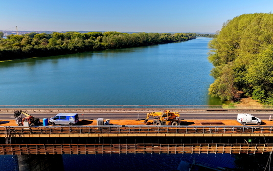 Aerial view of the Smederevo bridge over the Danube river with construction machinery and vehicles on the road surface surrounded by lush green trees in Smederevo Podunavlje District Serbia.