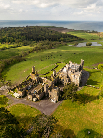 Aerial view of Castlefreke Castle a historic stone structure with ruined sections and towers set amidst lush green fields and rolling hills in Castlefreke County Cork Ireland.