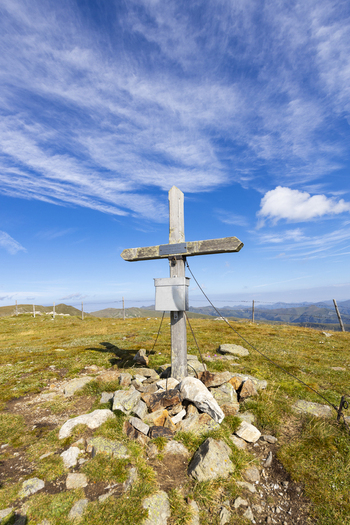 View of a weathered wooden cross stands sentinel atop a grassy hill under a sky streaked with cirrus clouds evoking solitude and reverence Lachtal Styria Austria. View of a weathered wooden cross stands sentinel atop a grassy hill under a sky streaked with cirrus clouds evoking solitude and reverence Lachtal Styria Austria.