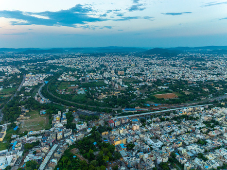 Aerial view of the sprawling cityscape of Udaipur with dense residential rooftops winding roads and lush green patches under a soft twilight sky in Udaipur Rajasthan India.