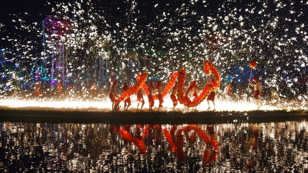 View of performers executing a traditional dragon dance with molten iron sparks creating a brilliant display of light reflected in the water in Wuhan China.