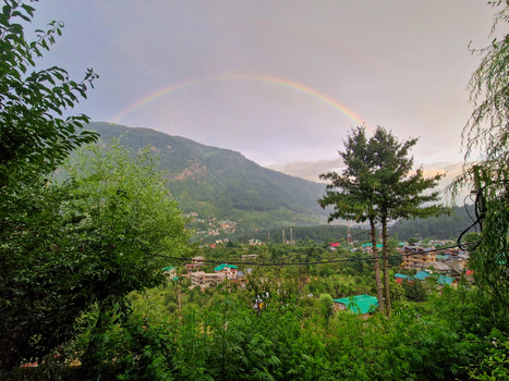 View of a rainbow arching over the lush green mountains and village houses in Malana Himachal Pradesh India.