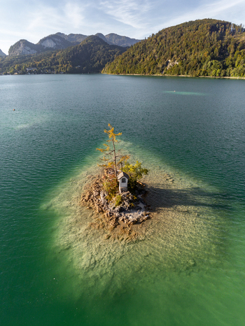 Aerial view of the Ochsenkreuz shrine on a small island in the clear water of the lake surrounded by mountains in Salzburg Umgebung Salzburg Austria.