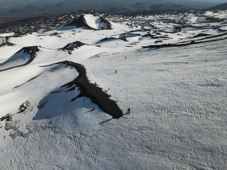 Aerial view of the snow covered southern slope of Mount Etna with volcanic craters and hikers walking across the white landscape in Nicolosi Sicilia Italy. Aerial view of the snow covered southern slope of Mount Etna with volcanic craters and hikers walking across the white landscape in Nicolosi Sicilia Italy.