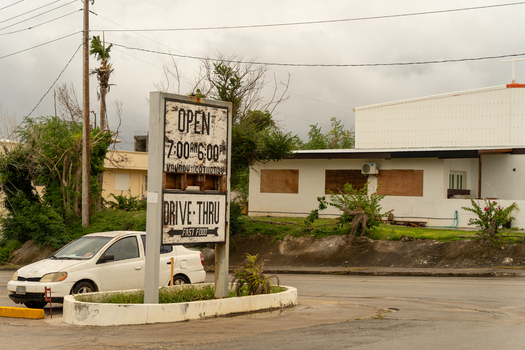 San Jose Tinian Northern Mariana Islands 05 July 2026 View of a weathered drive thru sign and a white car parked in front of a building with boarded up windows. San Jose Tinian Northern Mariana Islands 05 July 2026 View of a weathered drive thru sign and a white car parked in front of a building with boarded up windows.