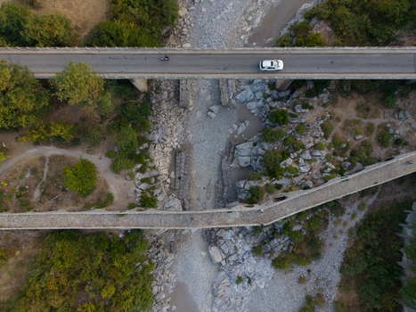 Aerial view of the historic Mesi Bridge spanning a dry rocky riverbed with a modern road bridge above in Boks Qarku i Shkodres Albania.