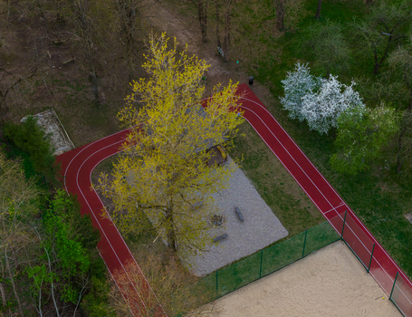 Aerial view of a red running track winding around a gravel recreation area with a large tree and a sand sports court in Vilnius County Lithuania. Aerial view of a red running track winding around a gravel recreation area with a large tree and a sand sports court in Vilnius County Lithuania.