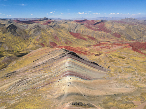 Aerial view of Vinicunca Rainbow Mountain showing vibrant mineral stripes and hikers on the ridge among rugged Andean peaks in Quispicanchi Province Cusco Peru.
