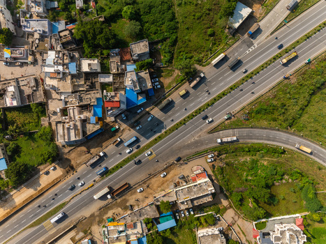Aerial view of a highway intersection with vehicles surrounded by urban buildings rooftops and green vegetation in Udaipur Rajasthan India. Aerial view of a highway intersection with vehicles surrounded by urban buildings rooftops and green vegetation in Udaipur Rajasthan India.