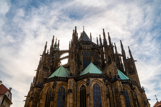 Prague Czechia 08 May 2023 View of St. Vitus Cathedral featuring intricate Gothic architecture pointed spires and green copper roofs set against a cloudy sky.