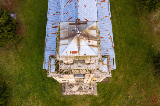 Aerial view of the historic Palendriai church tower with its rusted metal roof and stone architecture surrounded by green fields in Palendriai Siauliu apskritis Lithuania.