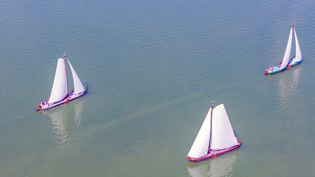 Aerial view of three traditional Dutch sailing boats gliding across the water in Heeg Friesland Netherlands. Aerial view of three traditional Dutch sailing boats gliding across the water in Heeg Friesland Netherlands.