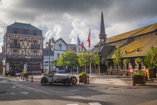 Aerial view of a vintage car parked in a town square with half timbered buildings under a cloudy sky &Eacute;tretat Normandy France.
