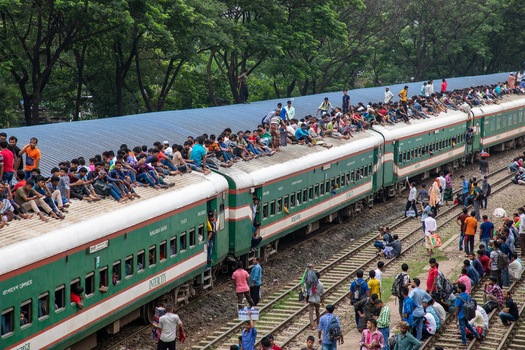 Dhaka Bangladesh 14 June 2018 View of Airport Railway Station with passengers crowded on the roofs of train carriages and standing along the tracks under lush green trees. Dhaka Bangladesh 14 June 2018 View of Airport Railway Station with passengers crowded on the roofs of train carriages and standing along the tracks under lush green trees.
