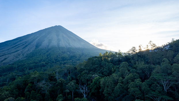 Aerial view of Mount Inerie volcano surrounded by lush green forests and a conical peak under soft morning light in Inerie East Nusa Tenggara Indonesia.