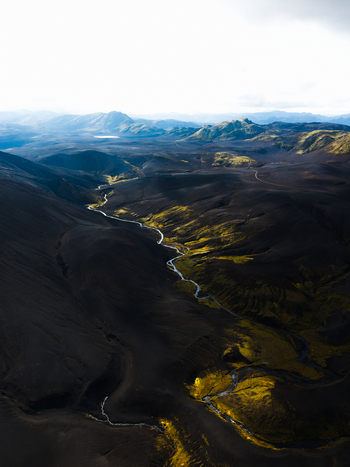 Aerial view of the rugged dark volcanic landscape is pierced by a serpentine river of pale green moss Iceland. Aerial view of the rugged dark volcanic landscape is pierced by a serpentine river of pale green moss Iceland.