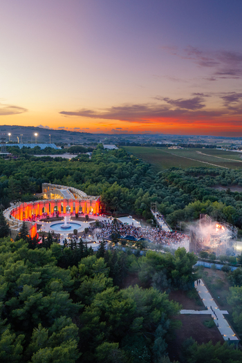 Aerial view of Park Nazzjonali Ta Qali at sunset featuring an illuminated amphitheater with a fountain and crowd surrounded by trees and fields in Attard Northern Region Malta. Aerial view of Park Nazzjonali Ta Qali at sunset featuring an illuminated amphitheater with a fountain and crowd surrounded by trees and fields in Attard Northern Region Malta.