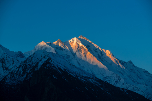 View of the snow capped peak of Rakaposhi mountain glowing under the golden hour light against a clear blue sky in Hunza Nagar Gilgit Pakistan. View of the snow capped peak of Rakaposhi mountain glowing under the golden hour light against a clear blue sky in Hunza Nagar Gilgit Pakistan.