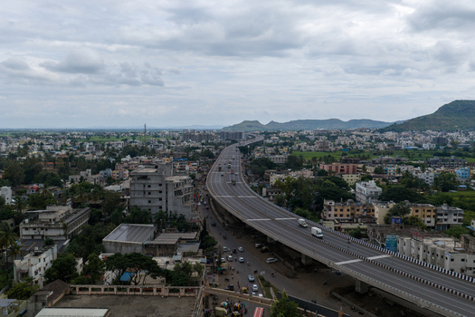 Aerial view of the highway flyover passing through the urban landscape with surrounding buildings lush greenery and distant hills under a cloudy sky Karad Maharashtra India.