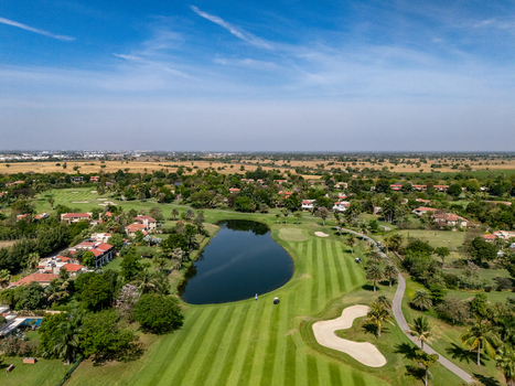 Ahmedabad Gujarat India 21 March 2026 Aerial view of Kalhaar Blues Greens Golf Club with lush fairways a central pond sand bunkers and villas under a clear blue sky.