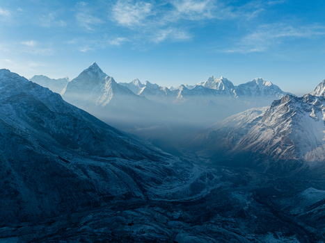 Aerial view of the snow capped Himalayan mountain range with misty valleys and rugged terrain under a clear blue sky in Nepal.