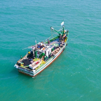 Aerial view of a fishing boat with fishermen working on deck surrounded by turquoise sea water in Ghana. Aerial view of a fishing boat with fishermen working on deck surrounded by turquoise sea water in Ghana.
