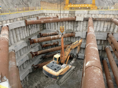 View of an excavator working inside a deep construction pit with large steel struts and concrete retaining walls in Avcilar Istanbul Turkiye. View of an excavator working inside a deep construction pit with large steel struts and concrete retaining walls in Avcilar Istanbul Turkiye.