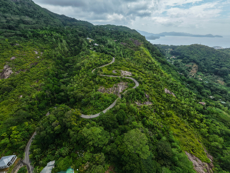 Aerial view of a winding road through lush tropical forest on the hills of Cap Ternay overlooking the coastline in Cap Ternay Port Glaud Seychelles. Aerial view of a winding road through lush tropical forest on the hills of Cap Ternay overlooking the coastline in Cap Ternay Port Glaud Seychelles.