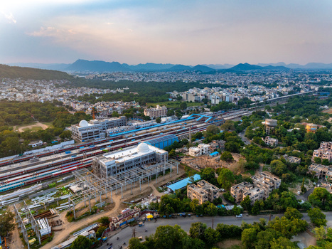 Aerial view of Udaipur railway station with multiple tracks trains surrounding urban buildings and distant hills under a soft golden hour sky in Udaipur Rajasthan India. Aerial view of Udaipur railway station with multiple tracks trains surrounding urban buildings and distant hills under a soft golden hour sky in Udaipur Rajasthan India.