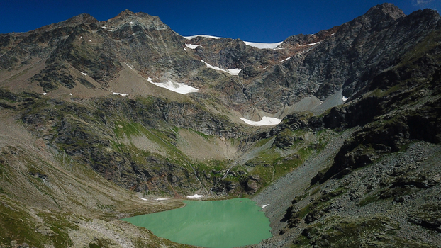 Aerial view of Lago di San Grato nestled amidst rugged rocky terrain and snow capped peaks under a clear blue sky Valgrisenche Aosta Valley Italy.
