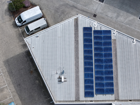 Aerial view of industrial building roof with solar panels and two white vans parked in the parking lot in Melbourne VIC Australia.