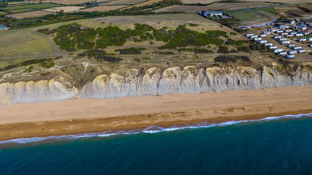 Aerial view of the dramatic sandstone cliffs and golden sandy beach at West Bay with a caravan park on the grassy clifftop in West Bay England United Kingdom. Aerial view of the dramatic sandstone cliffs and golden sandy beach at West Bay with a caravan park on the grassy clifftop in West Bay England United Kingdom.