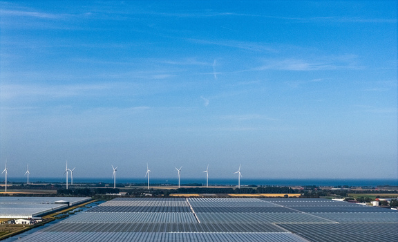 Aerial view of the Agriport A7 greenhouse complex with rows of wind turbines along the horizon under a clear blue sky in Middenmeer Noord Holland Netherlands. Aerial view of the Agriport A7 greenhouse complex with rows of wind turbines along the horizon under a clear blue sky in Middenmeer Noord Holland Netherlands.