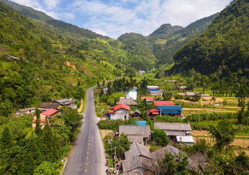 Aerial view of a rural road winding through a lush green valley with traditional houses terraced fields and surrounding mountains in Pho Bang Tuyen Quang Vietnam.